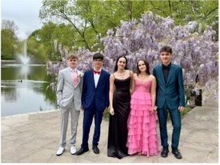 A group of students in tuxedos and prom dresses posing in front of a lake