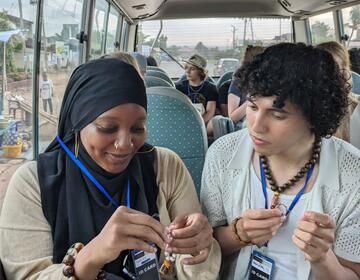Max looks on as Monajah finishes her beading on the bus.