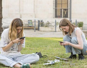 high schoolers on their phones outside in the grass