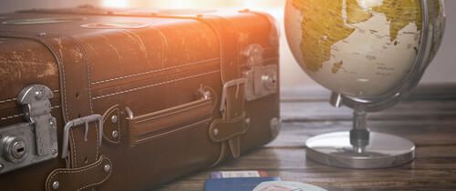 Globe and passport beside luggage on desk
