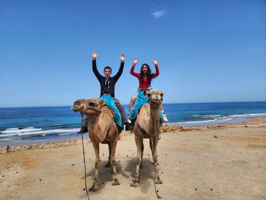 Two CIEE students sitting on camels with their arms raised