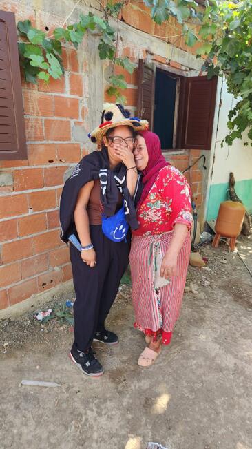 One of the students standing next to a Moroccan woman of the household and smiling