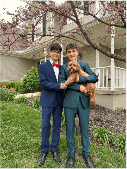 two male students dressed in formal suits holding a brown dog in front of a house - they are heading to prom