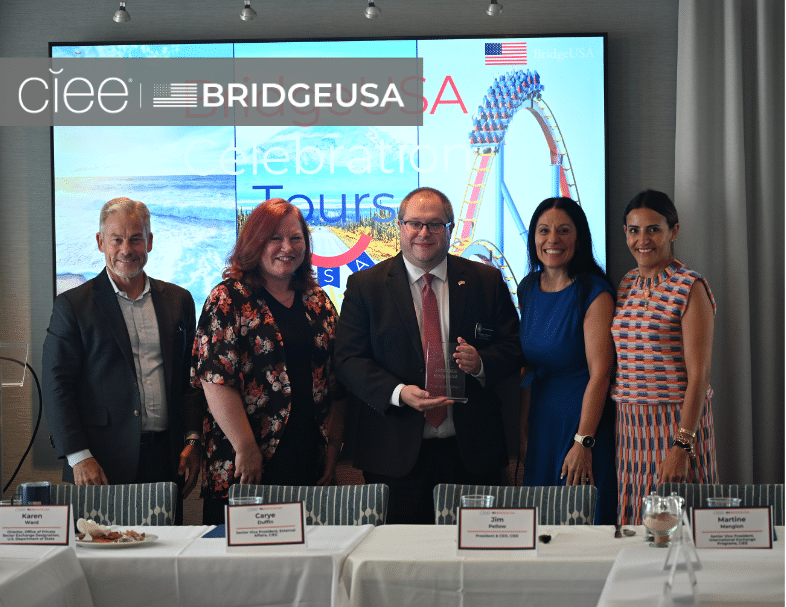 CIEE and BridgeUSA representatives pose with an award recipient holding a glass award at a BridgeUSA Celebration Tour event.
