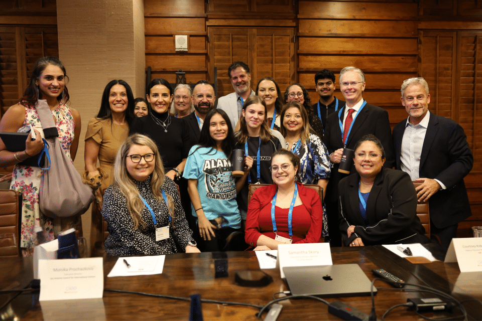 Group photo of CIEE senior leadership with San Antonio partners seated and standing around a conference table.